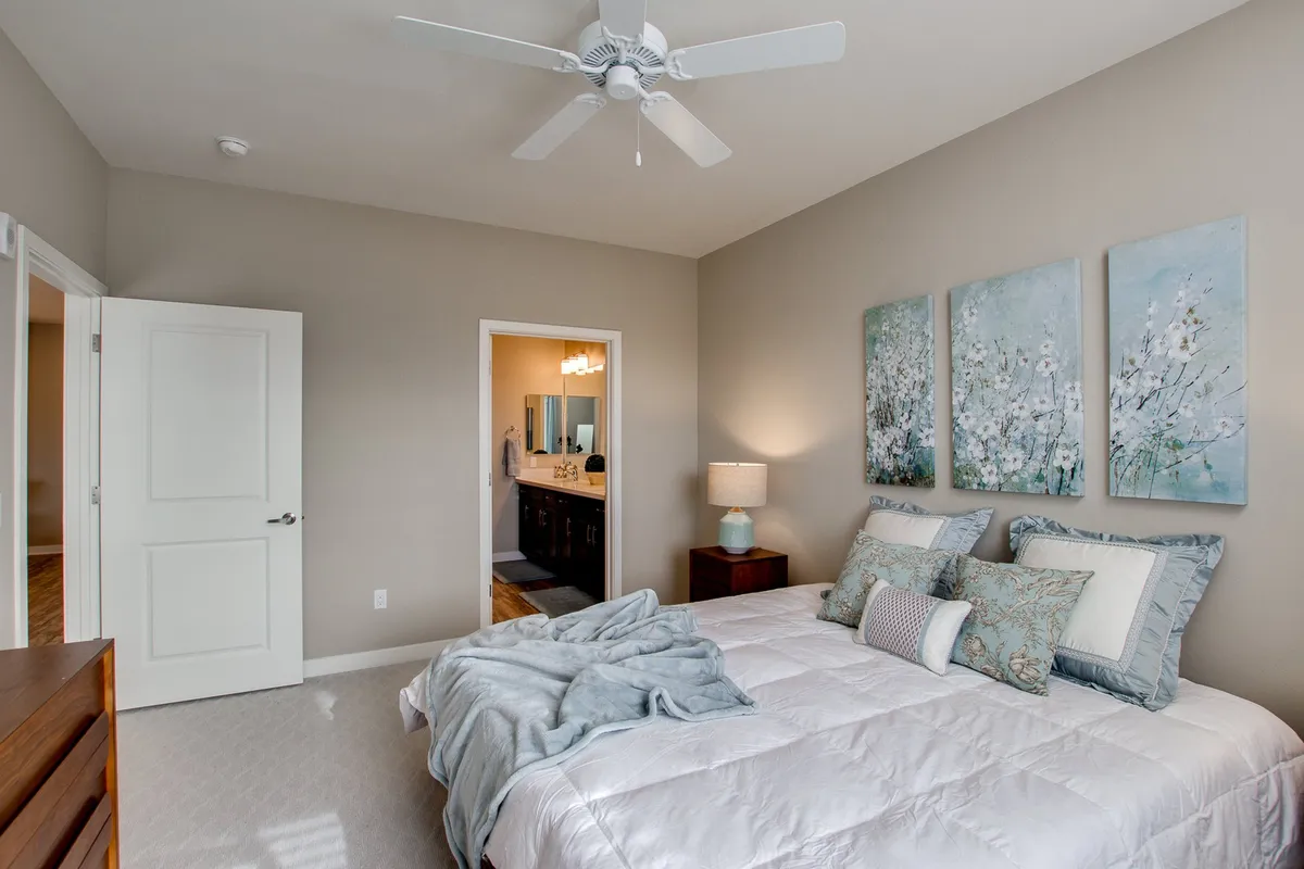 A serene and comfortable bedroom featuring a bed with decorative pillows, calming artwork on the wall, and a nightstand with a lamp. Natural light filters softly through the window, contributing to a tranquil atmosphere ideal for relaxation.