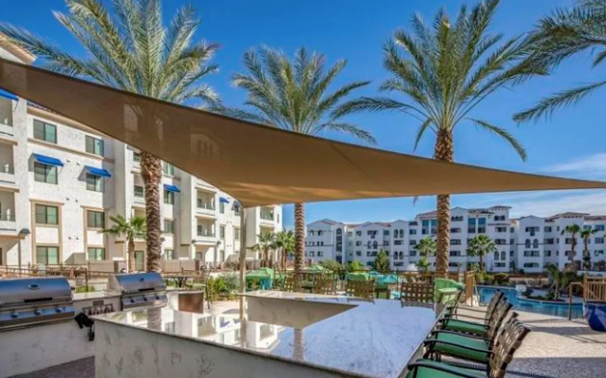 An outdoor kitchen area with built-in grills, palm trees, and a swimming pool set the scene for lively poolside barbecues. The area is designed for communal gatherings and leisure, with the pool providing a backdrop for relaxation and fun.
