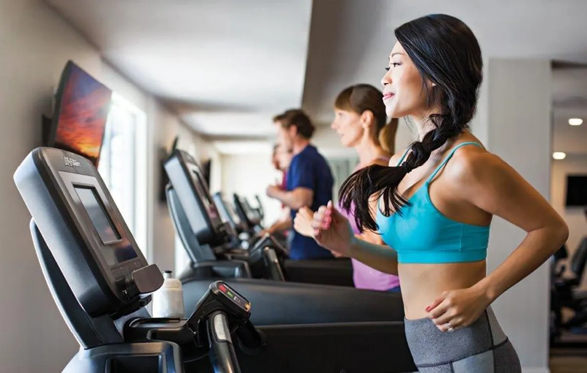 A modern fitness center featuring treadmills and exercisers, with screens displaying scenic views. The atmosphere is energetic and focused, ideal for those prioritizing health and activity during their stay.