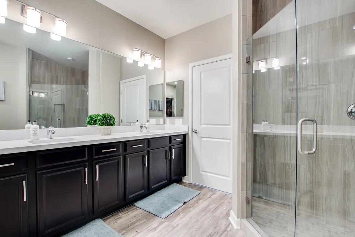 A modern bathroom with double vanity sinks, expansive mirrors, and a glass-enclosed shower. The space is bright, open, and evokes a spa-like tranquility ideal for self-care and relaxation.
