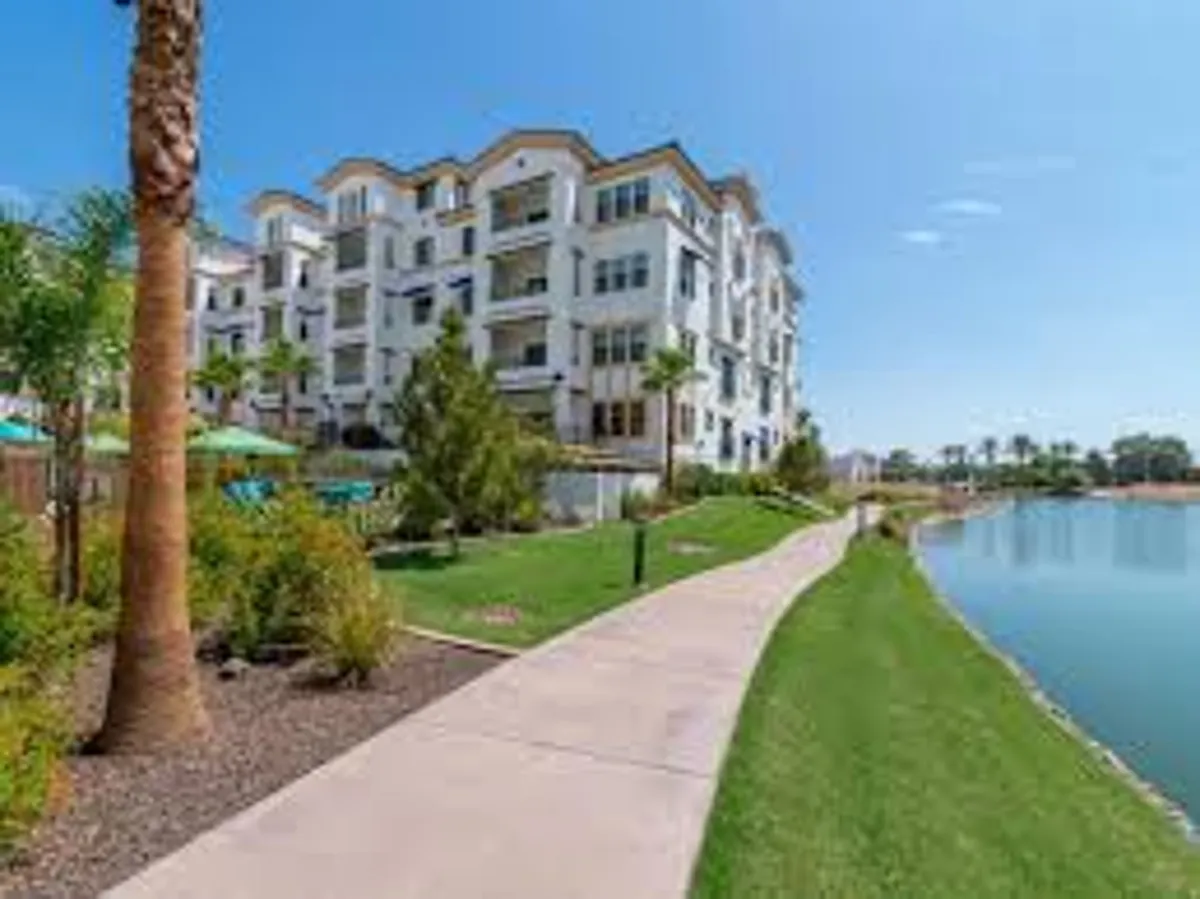 This image features a modern apartment building surrounded by landscaped gardens, a tranquil lake, and walking pathways. The setting is peaceful and inviting, emphasizing the overall ambiance of the community and its proximity to natural beauty.