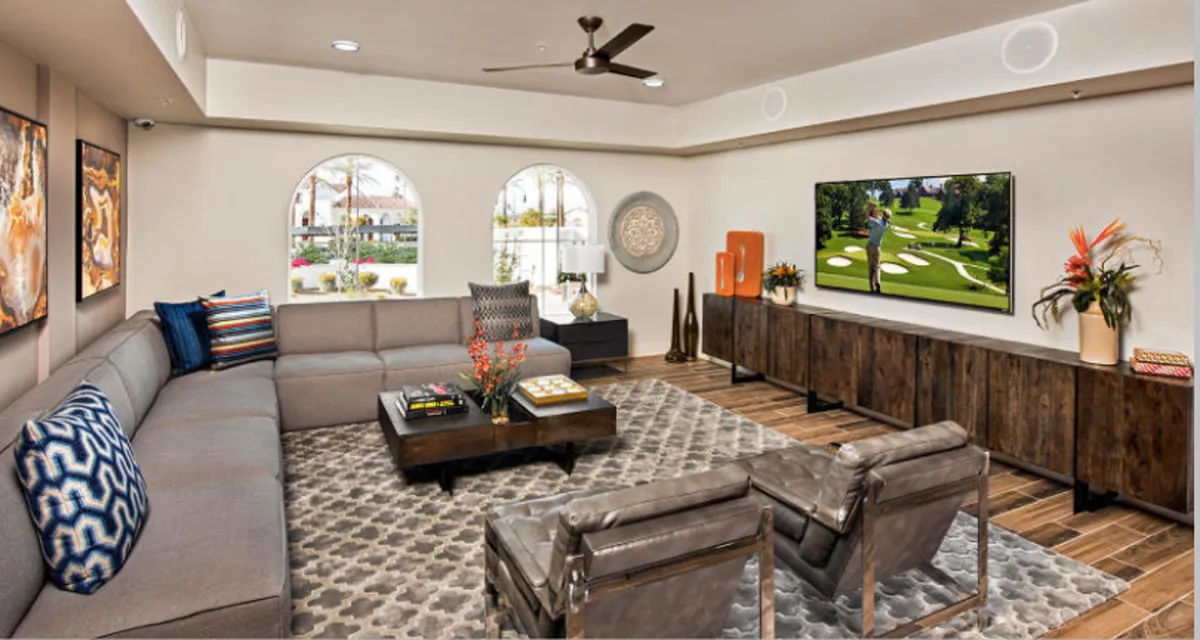 A spacious and relaxed living area featuring a large sectional sofa, a TV displaying a golf scene, decorative wall art, and a coffee table with magazines. The environment is casual, welcoming, and perfect for unwinding after returning home.